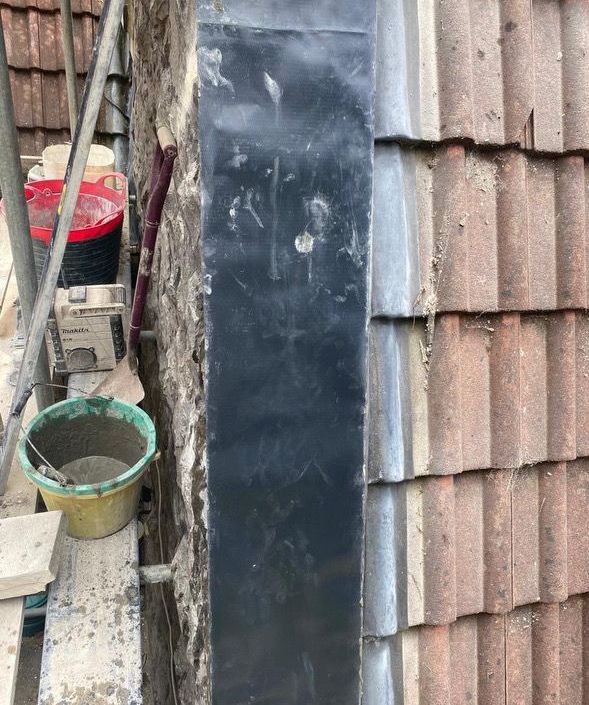 A bucket of cement is sitting on a scaffolding next to a brick wall.