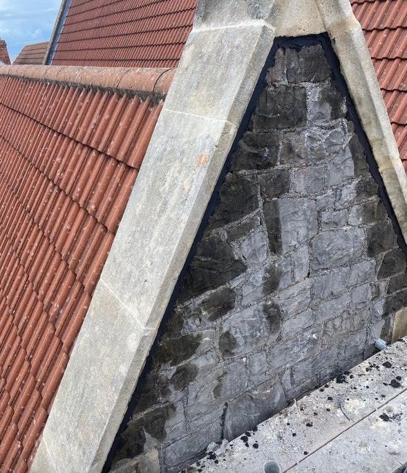 A brick chimney on top of a roof with red tiles.
