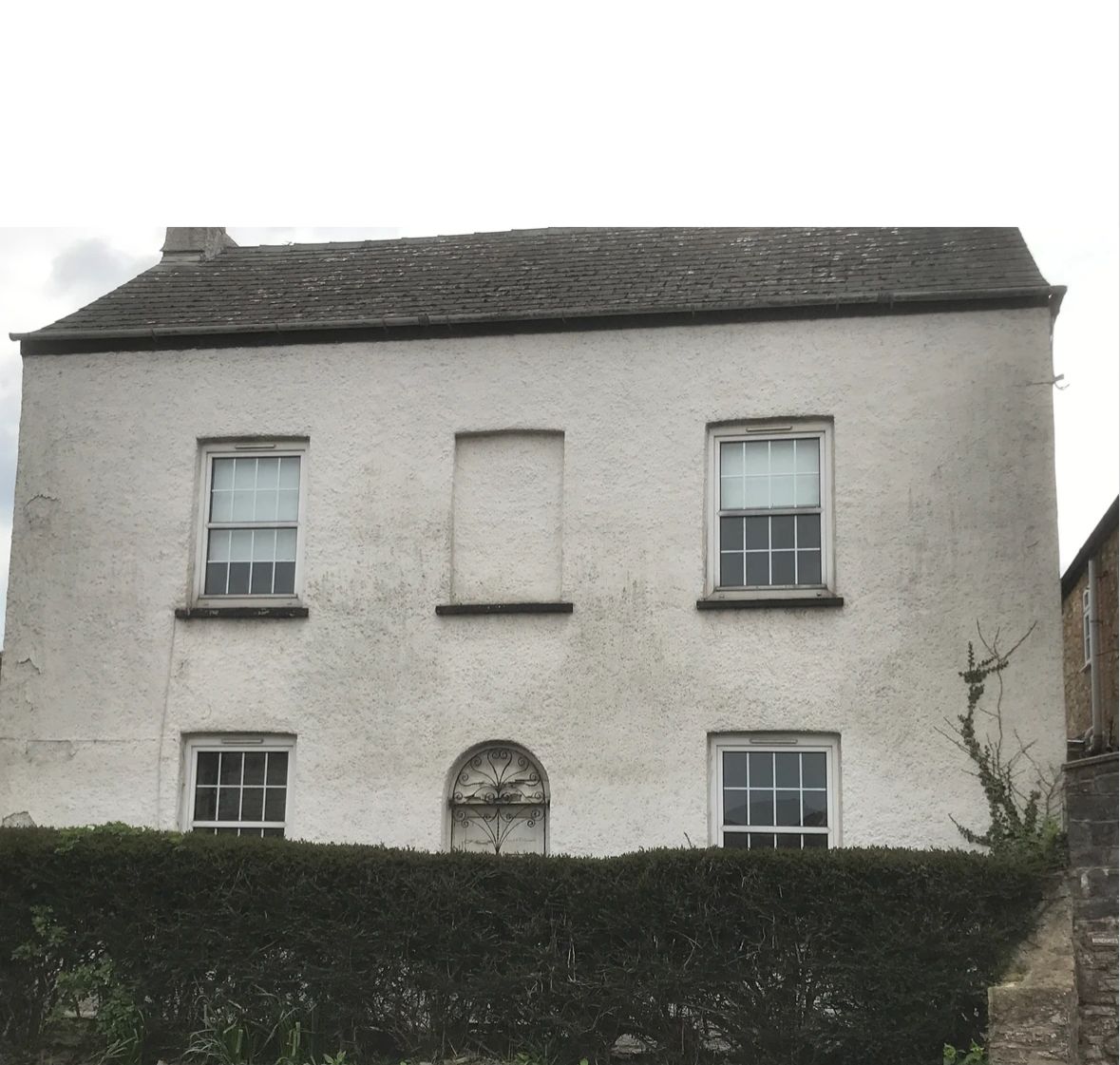 A large white house with a hedge in front of it