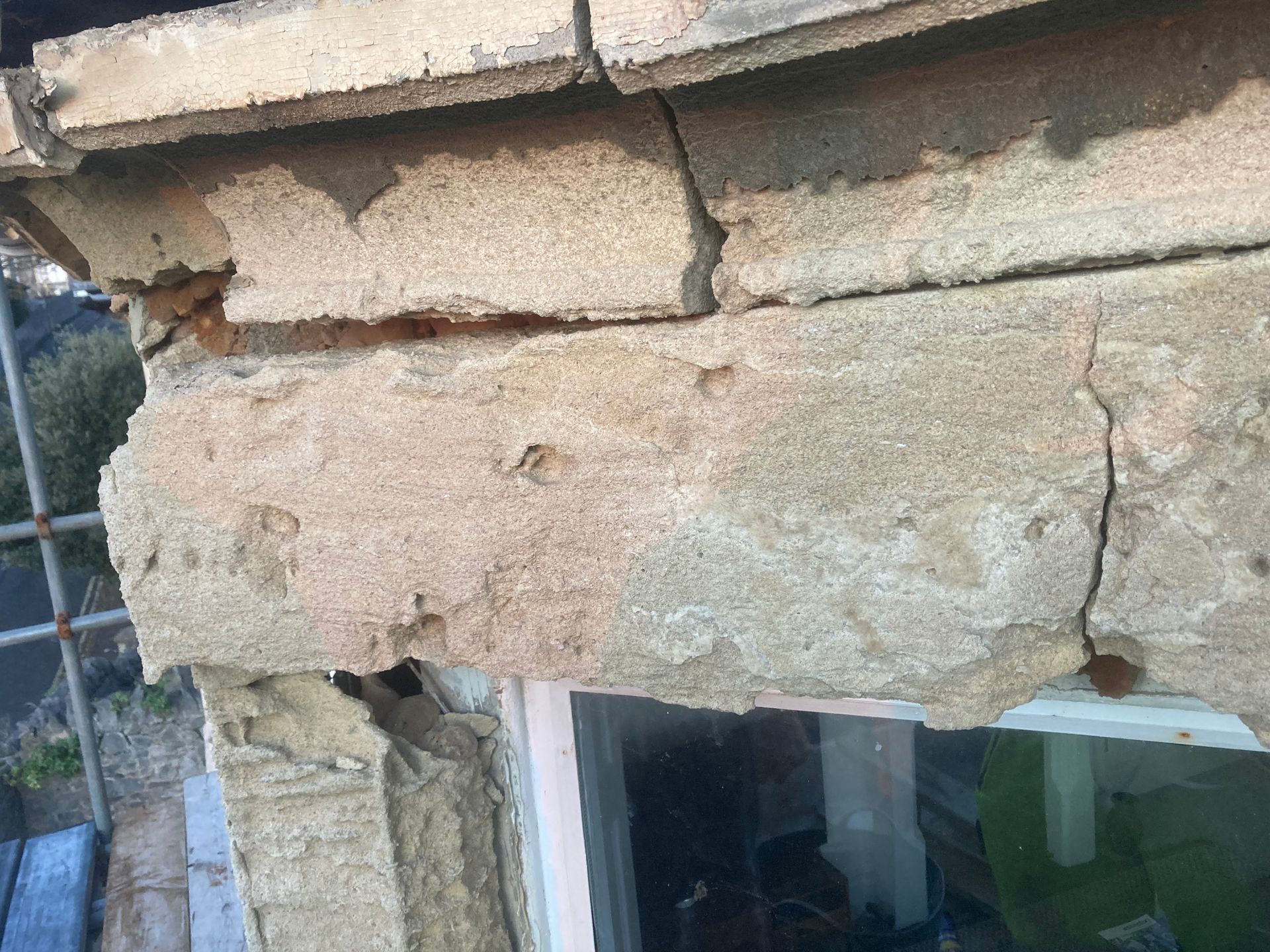 A close up of a cracked stone wall next to a window.