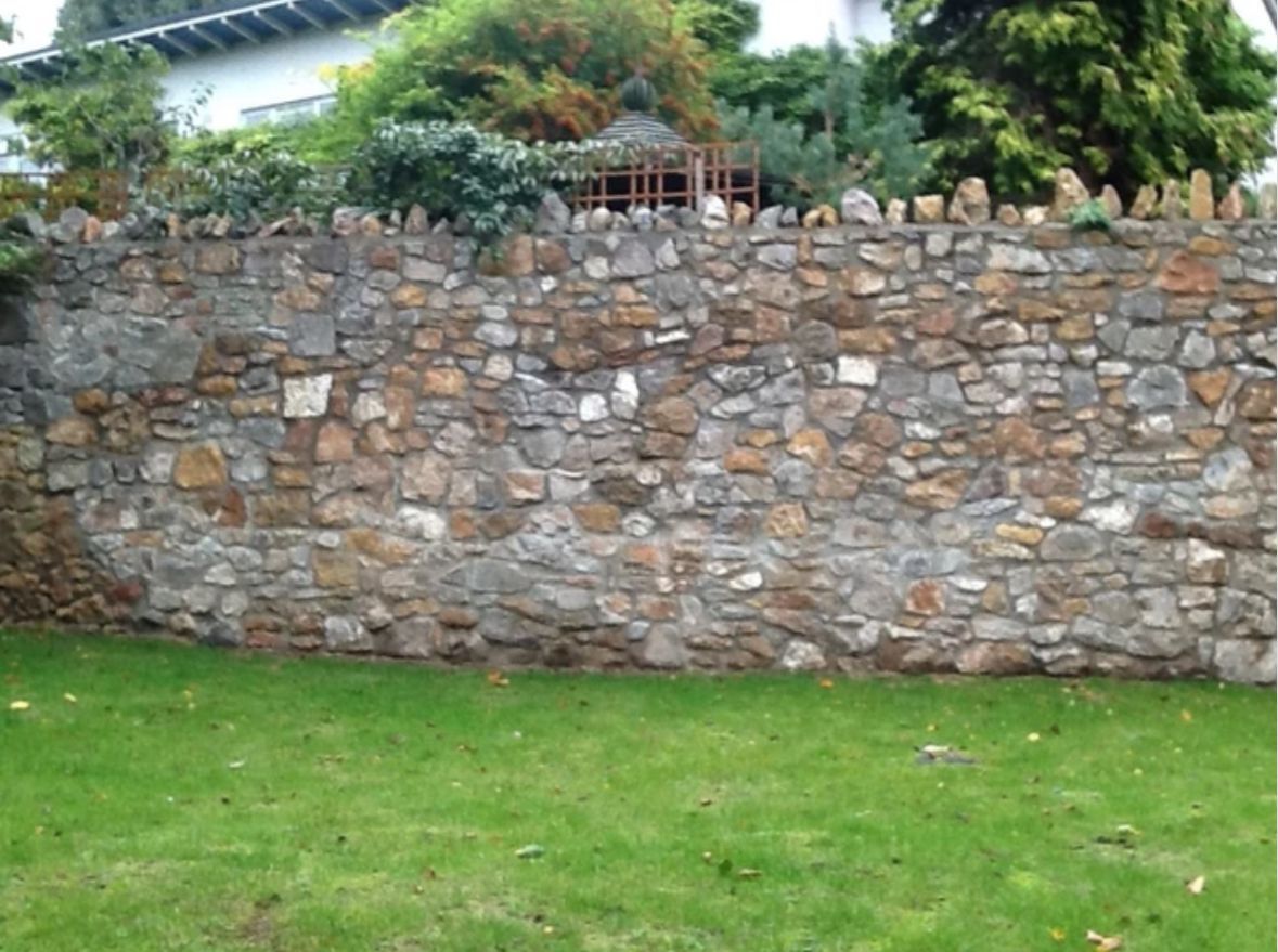 A large stone wall surrounds a lush green lawn.