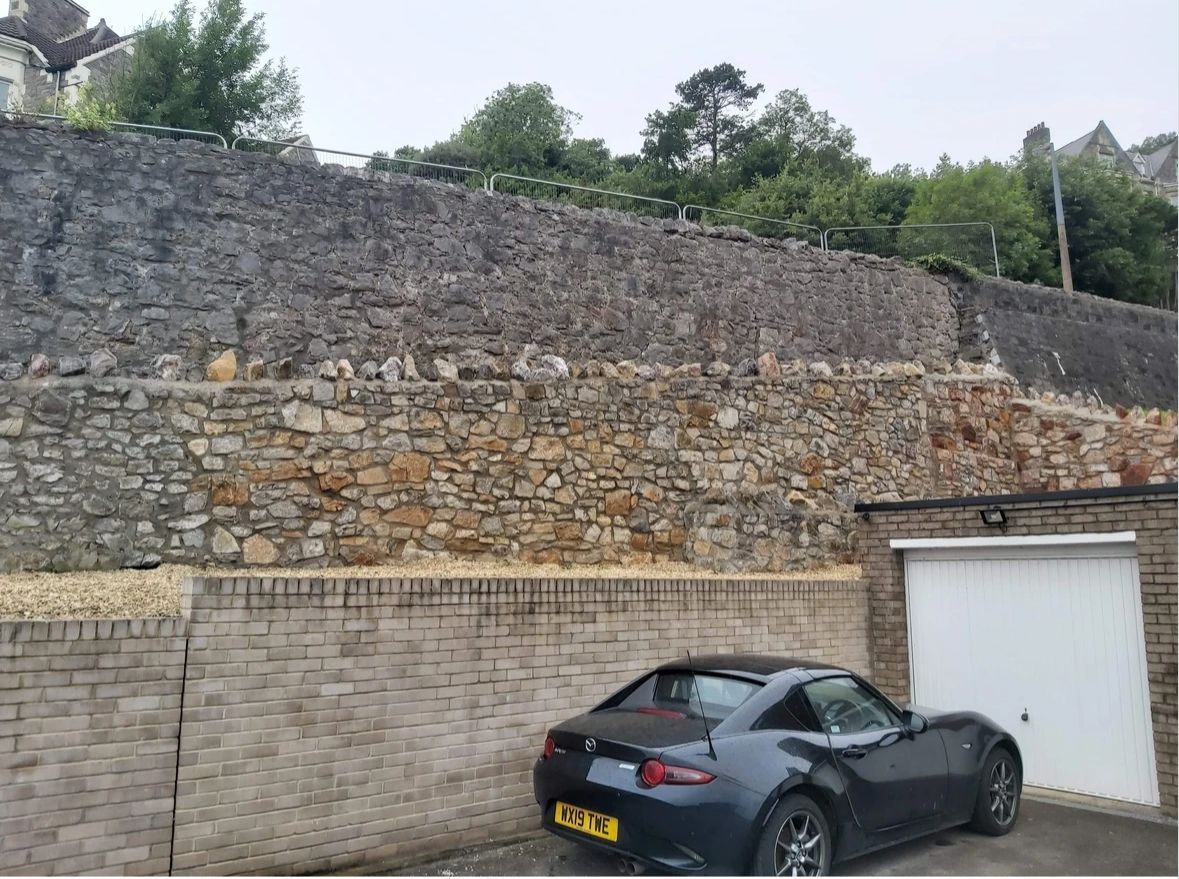 A black sports car is parked in front of a stone wall.