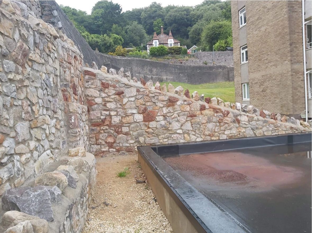 A large stone wall with a building in the background