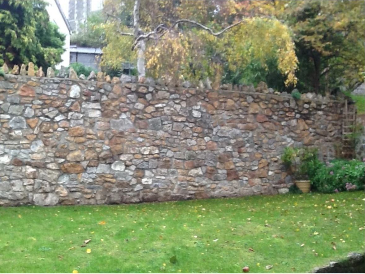 A large stone wall surrounds a lush green lawn.