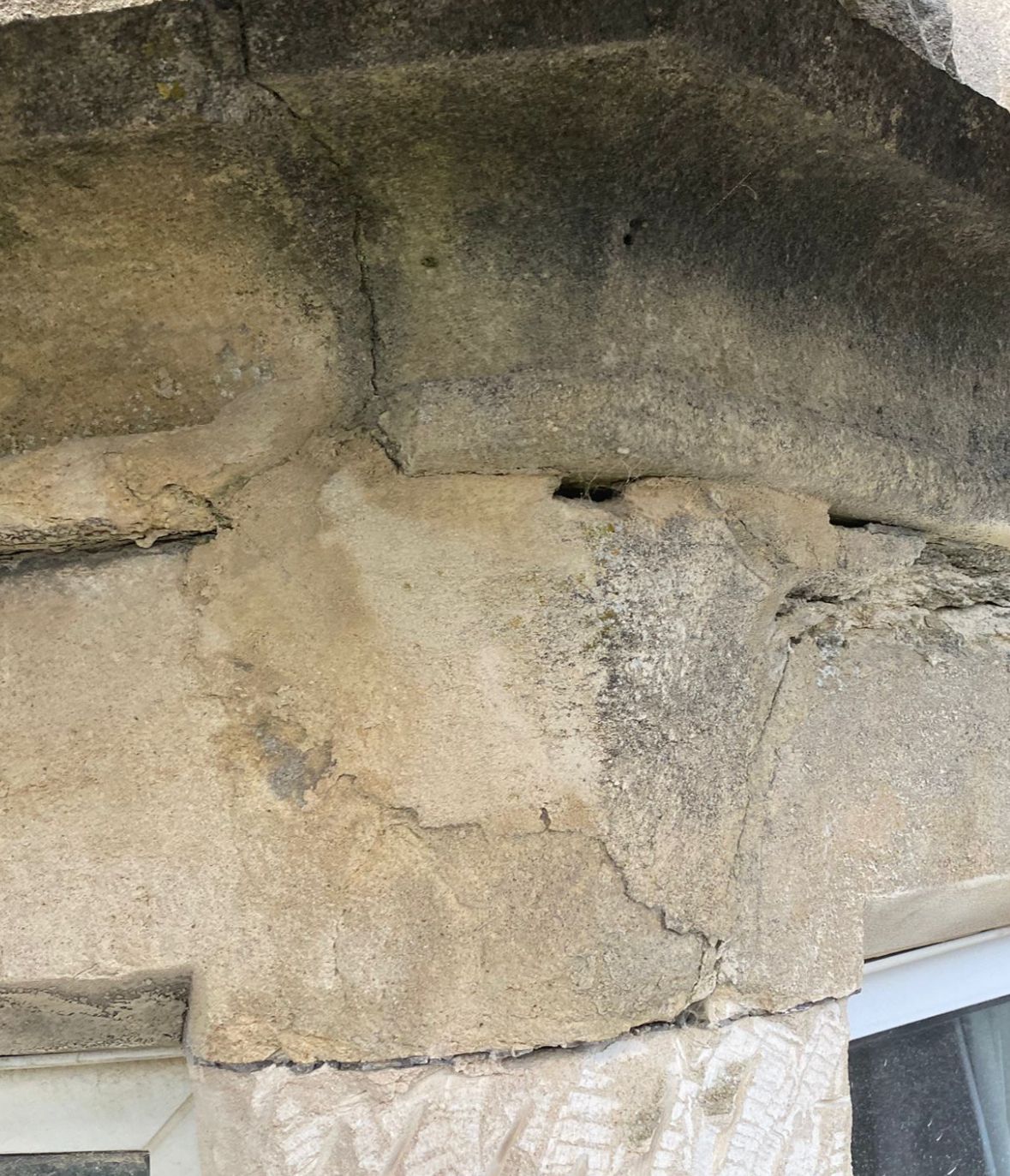 A close up of a cracked stone wall next to a window.