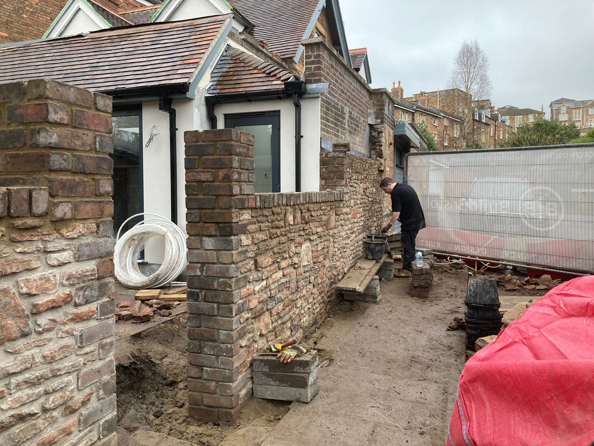 A man is working on a brick wall in front of a house.