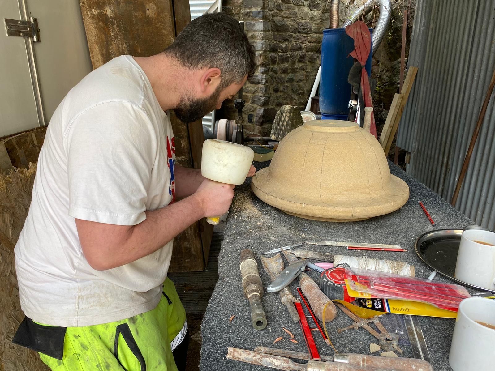 A man is working on a sculpture with a mallet.