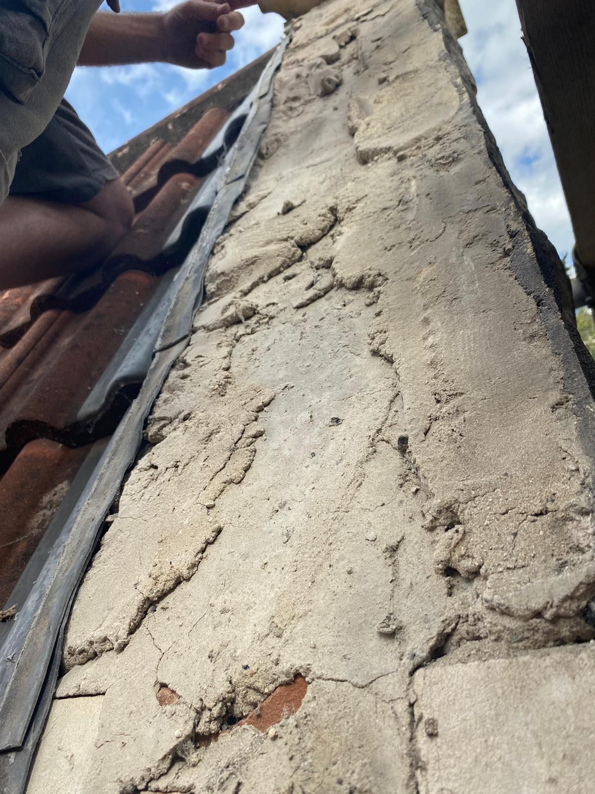 A person is working on a chimney on the roof of a building.