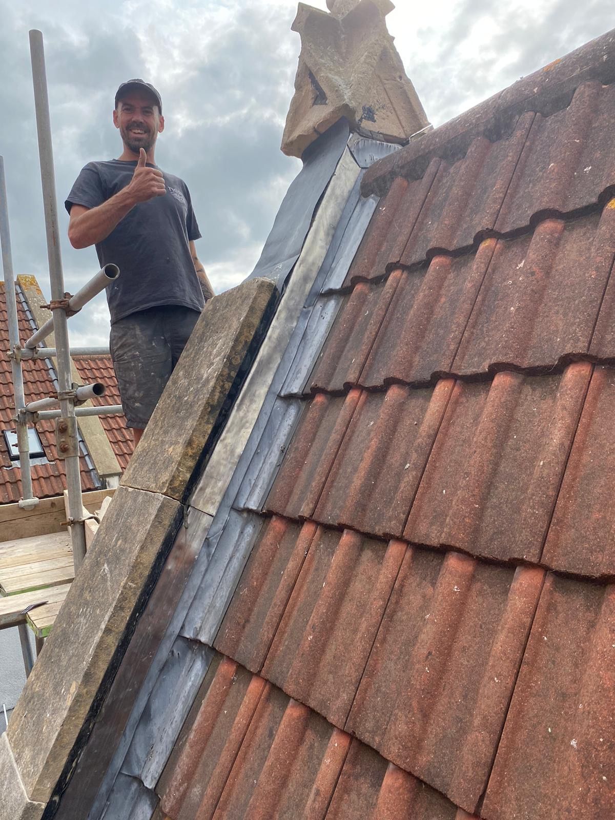 A man is standing on top of a tiled roof giving a thumbs up.