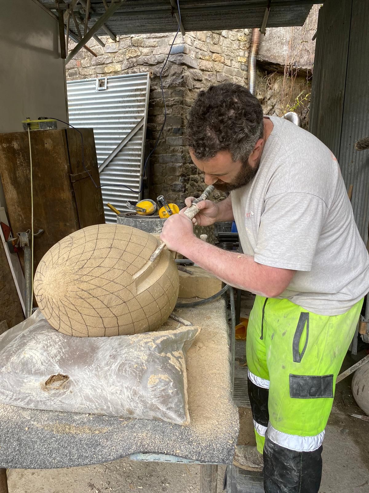A man in yellow pants is carving a stone sculpture.