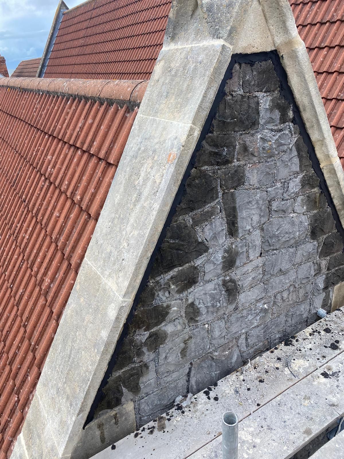 A brick chimney is sitting on top of a roof next to a scaffolding.