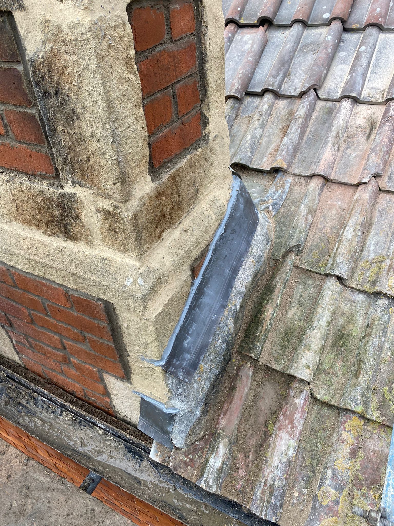 A brick chimney is sitting on top of a tiled roof.