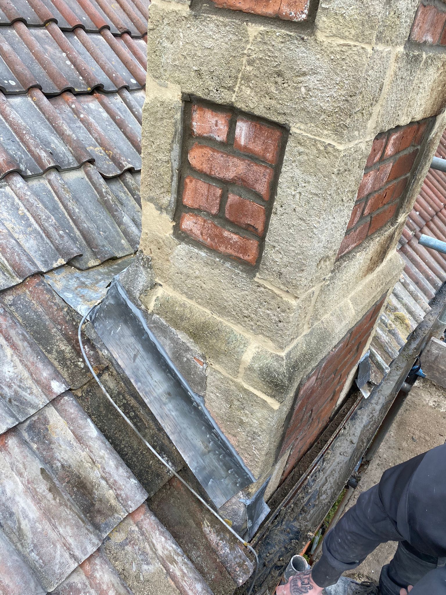 A person is working on a chimney on top of a roof.
