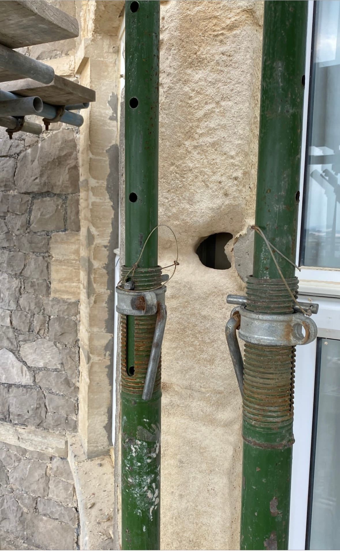 Two green pipes are attached to a wall next to a window.