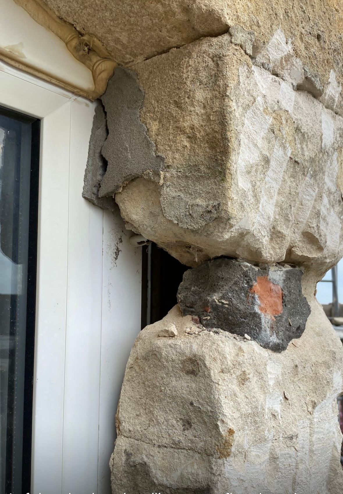 A large rock is sitting on top of a building next to a window.