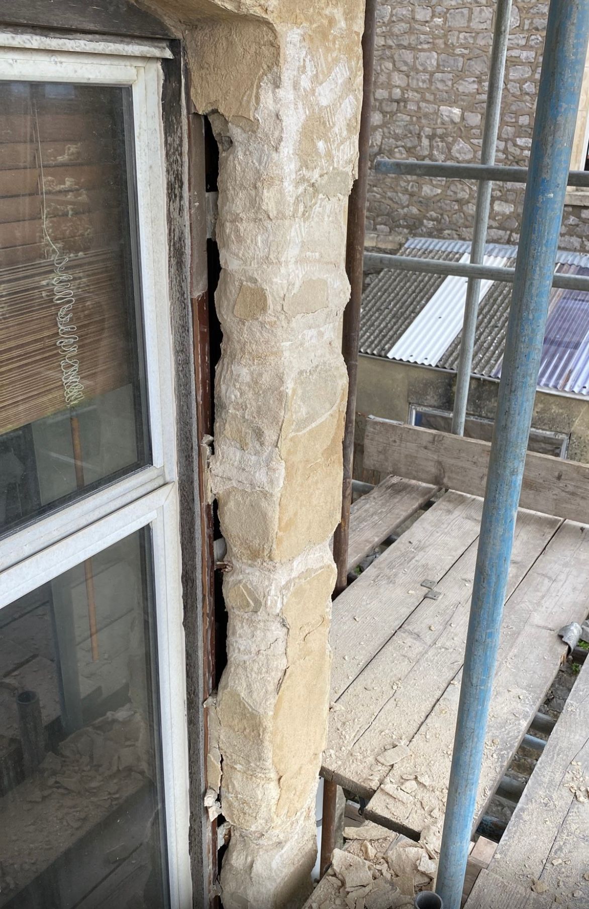 A window is sitting on top of a wooden scaffolding next to a stone wall.