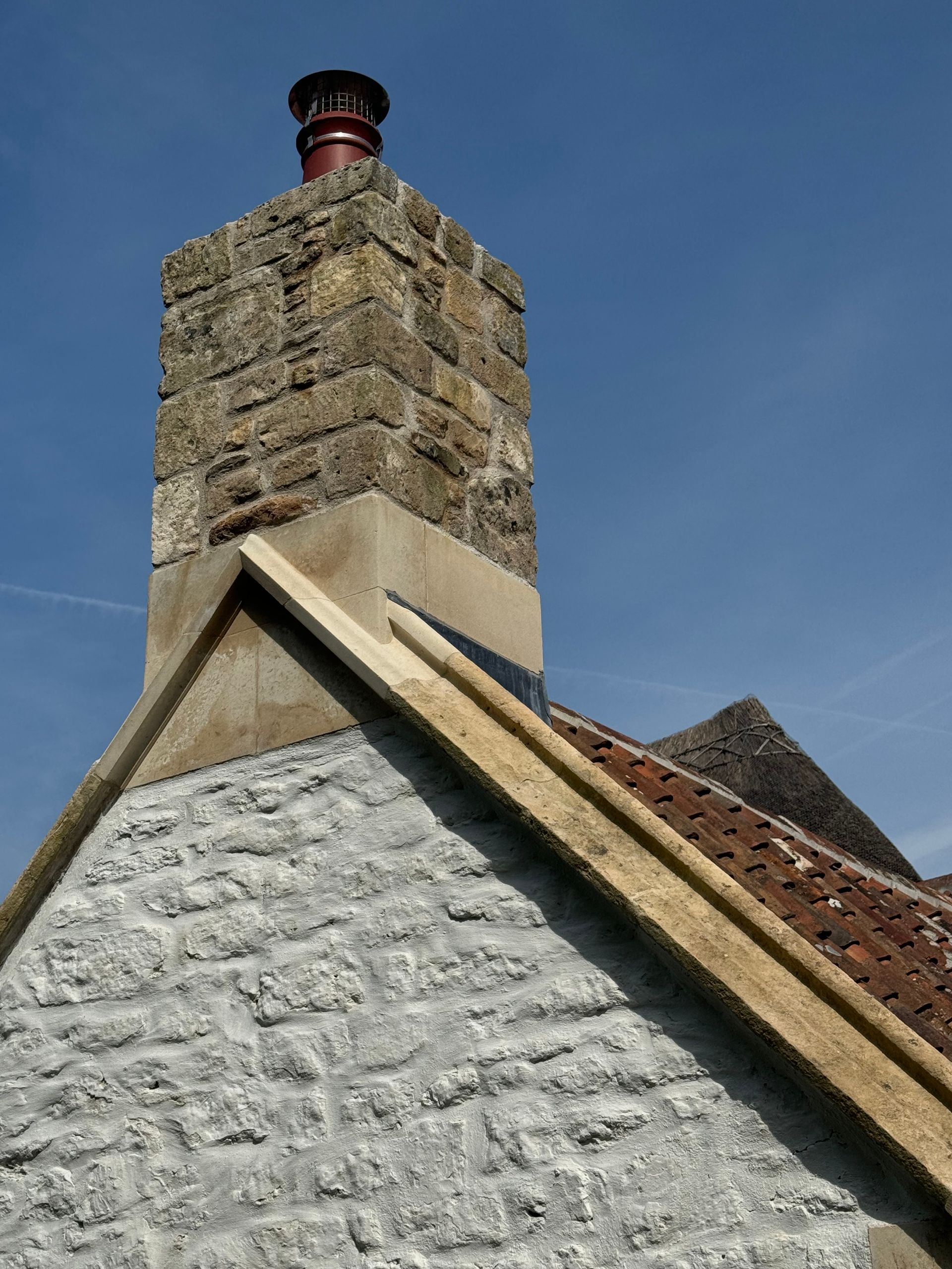 A chimney on top of a stone building with a blue sky in the background