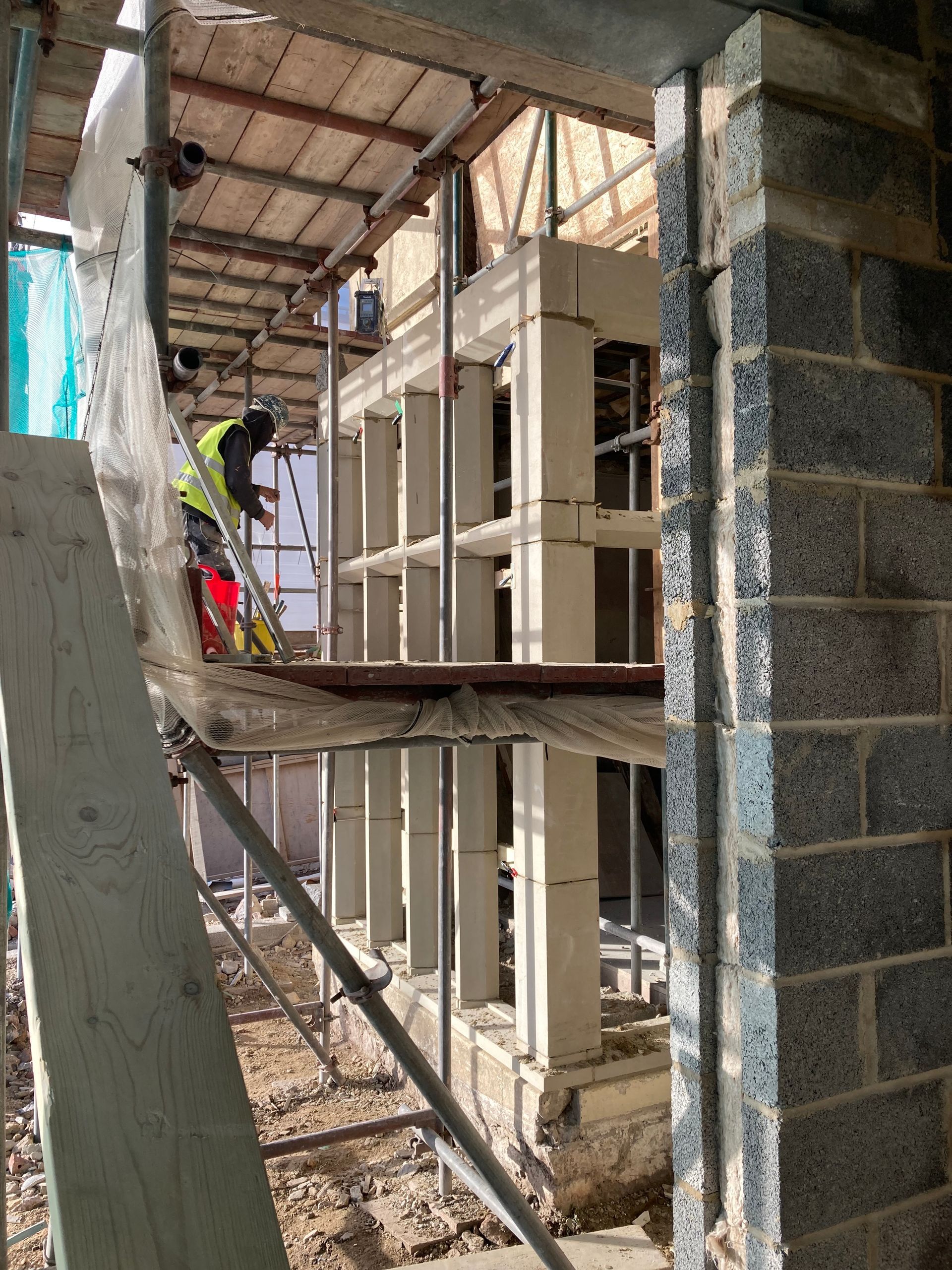 A man is standing on a scaffolding in front of a building under construction.