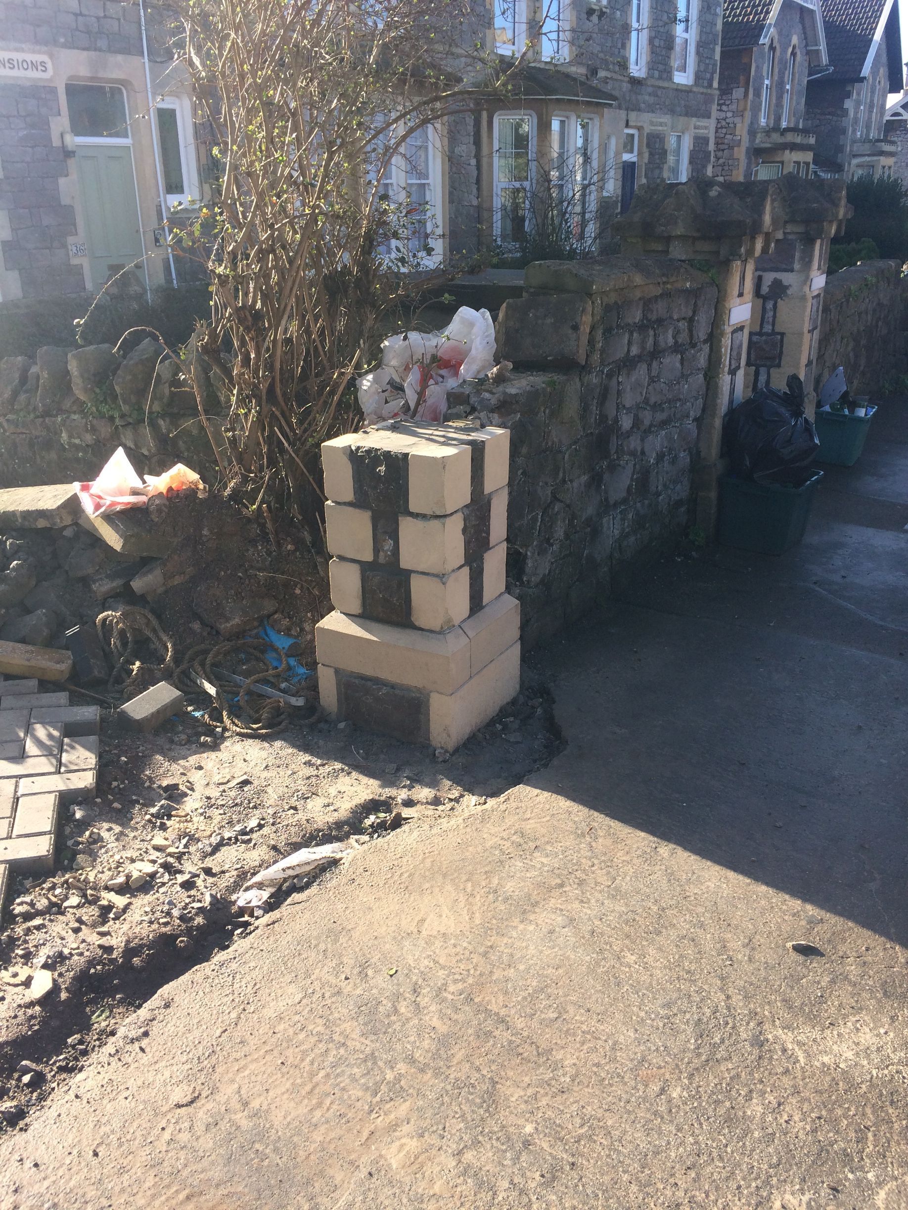A brick pillar is sitting on the side of a road in front of a building.