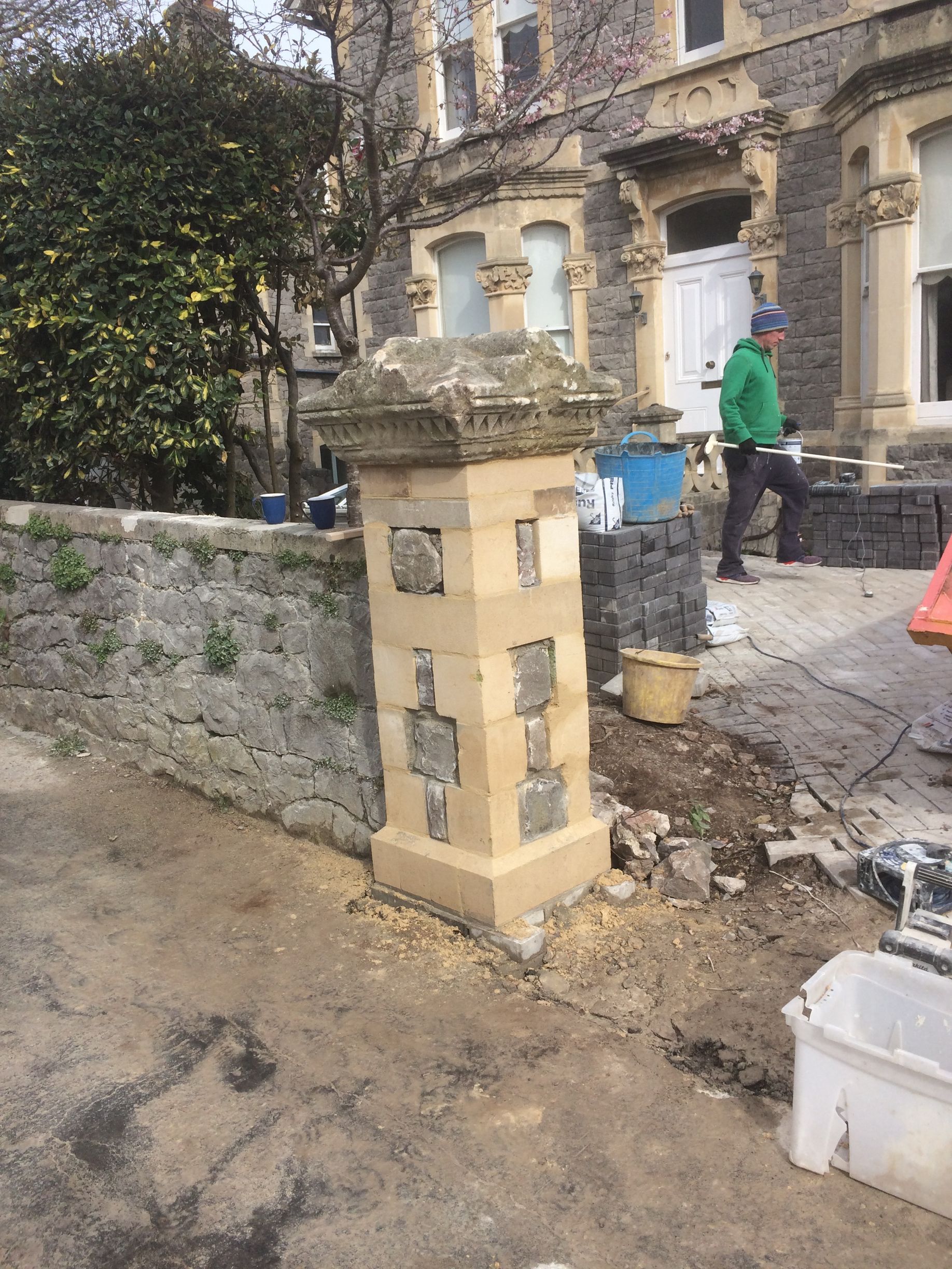 A man is standing next to a stone pillar in front of a building.