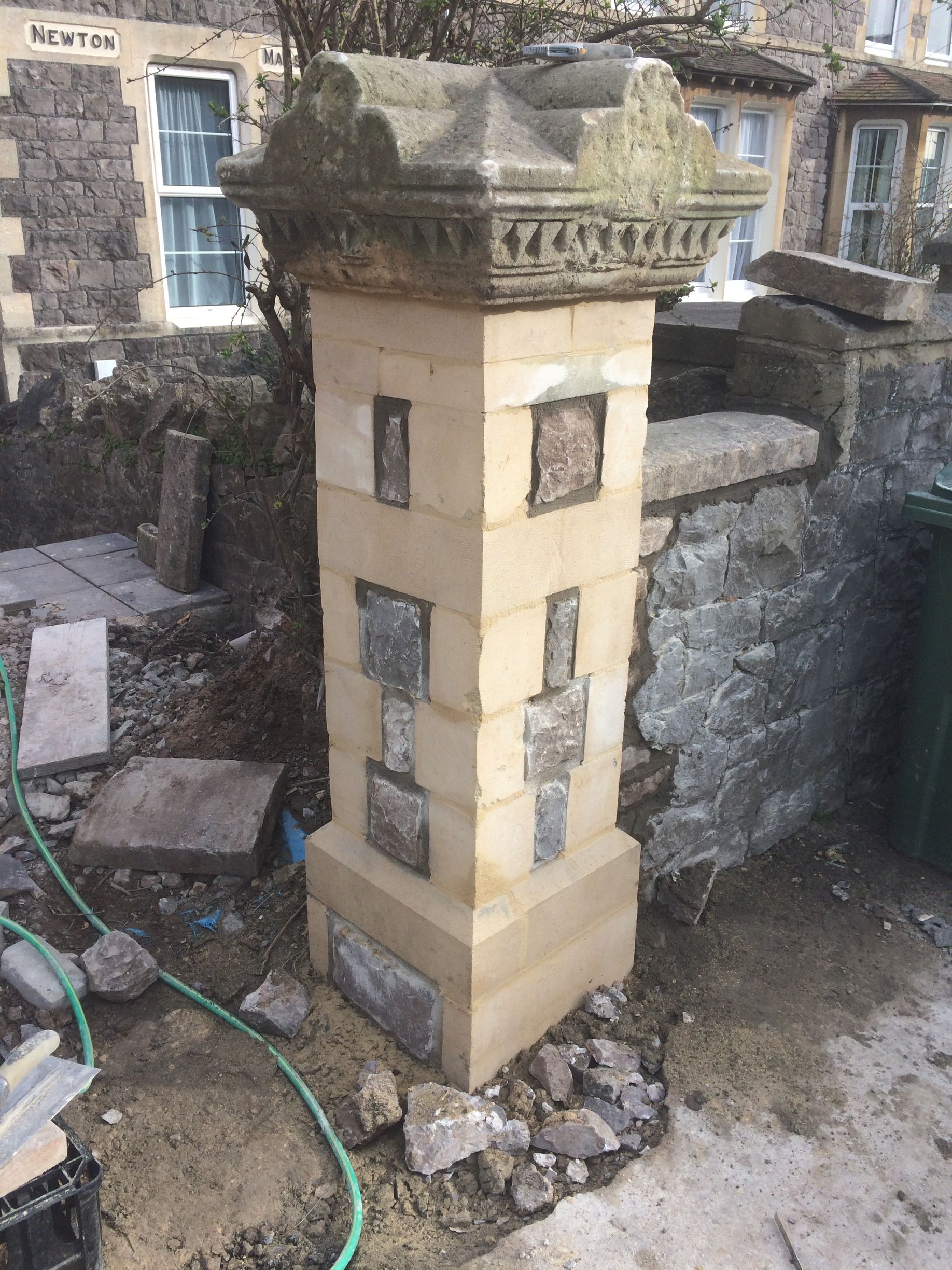A stone column is sitting in the dirt in front of a stone wall.