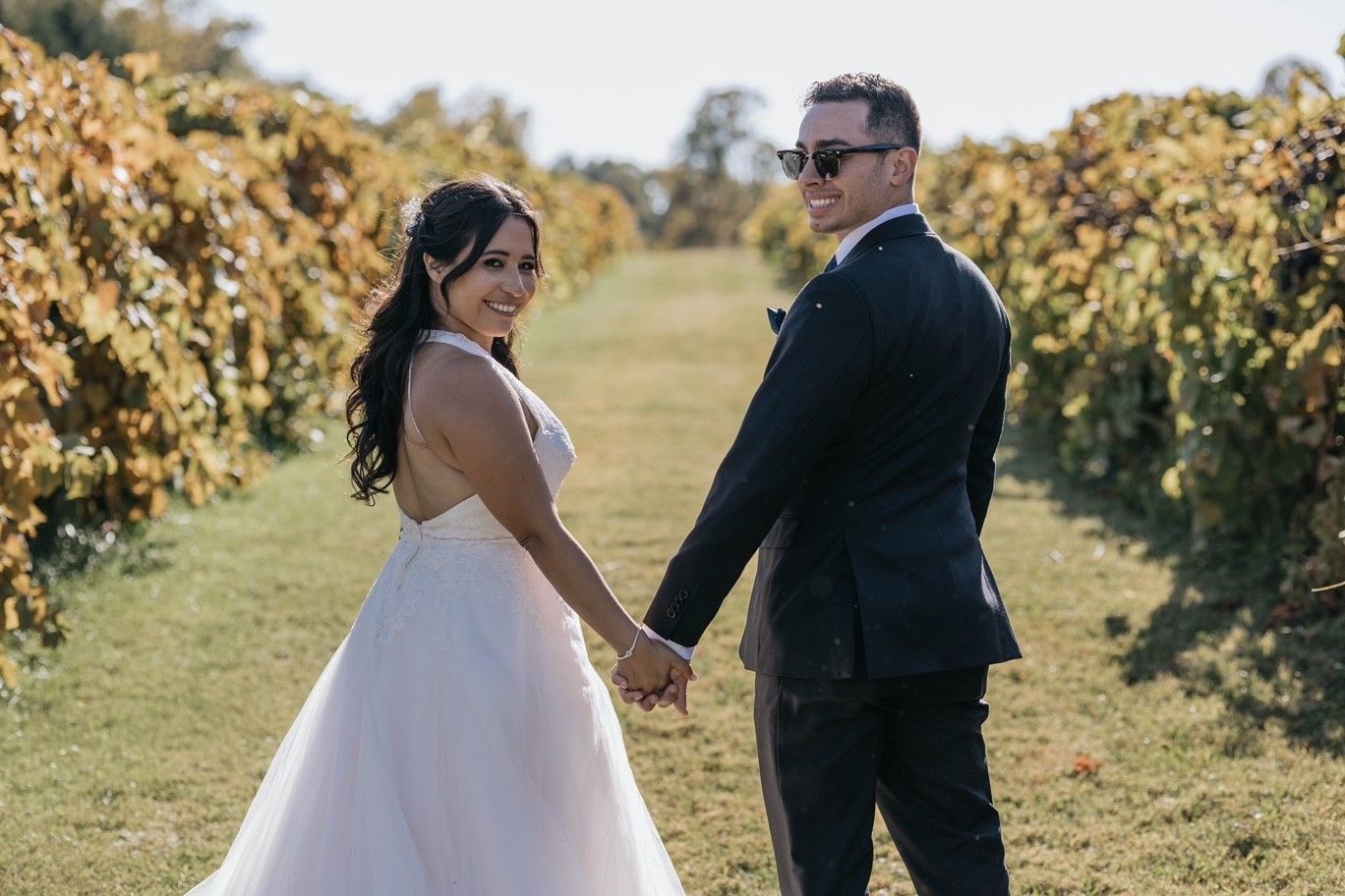 A bride and groom are holding hands in a vineyard.