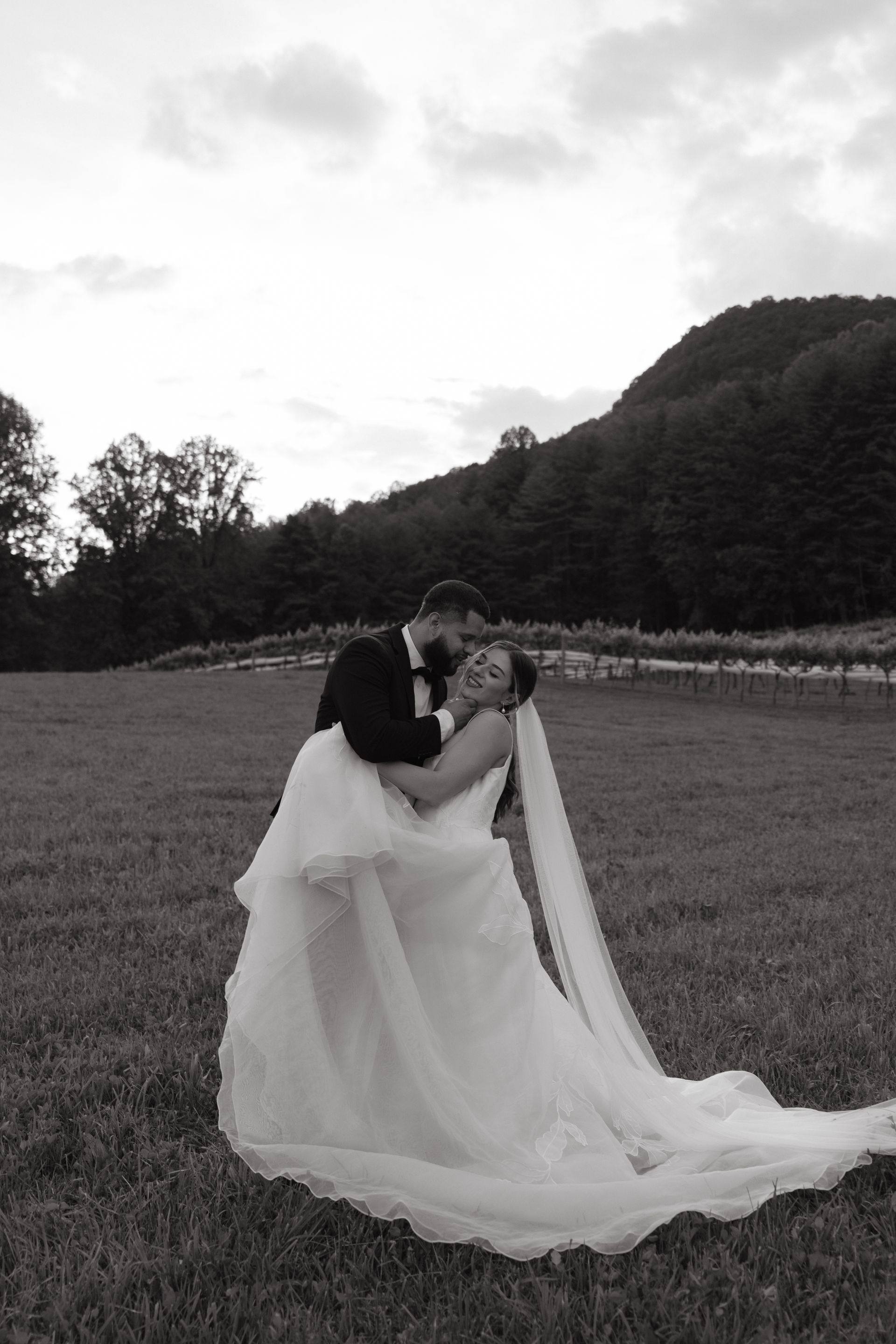 A bride and groom are kissing in a field in a black and white photo.