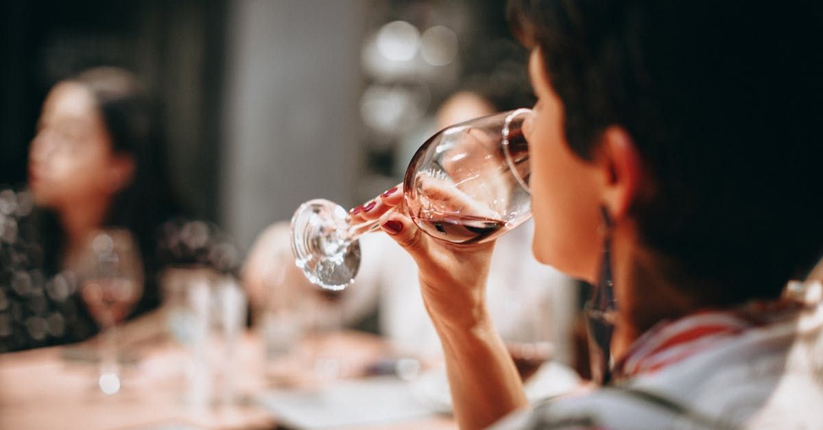 A woman is drinking a glass of red wine while sitting at a table.
