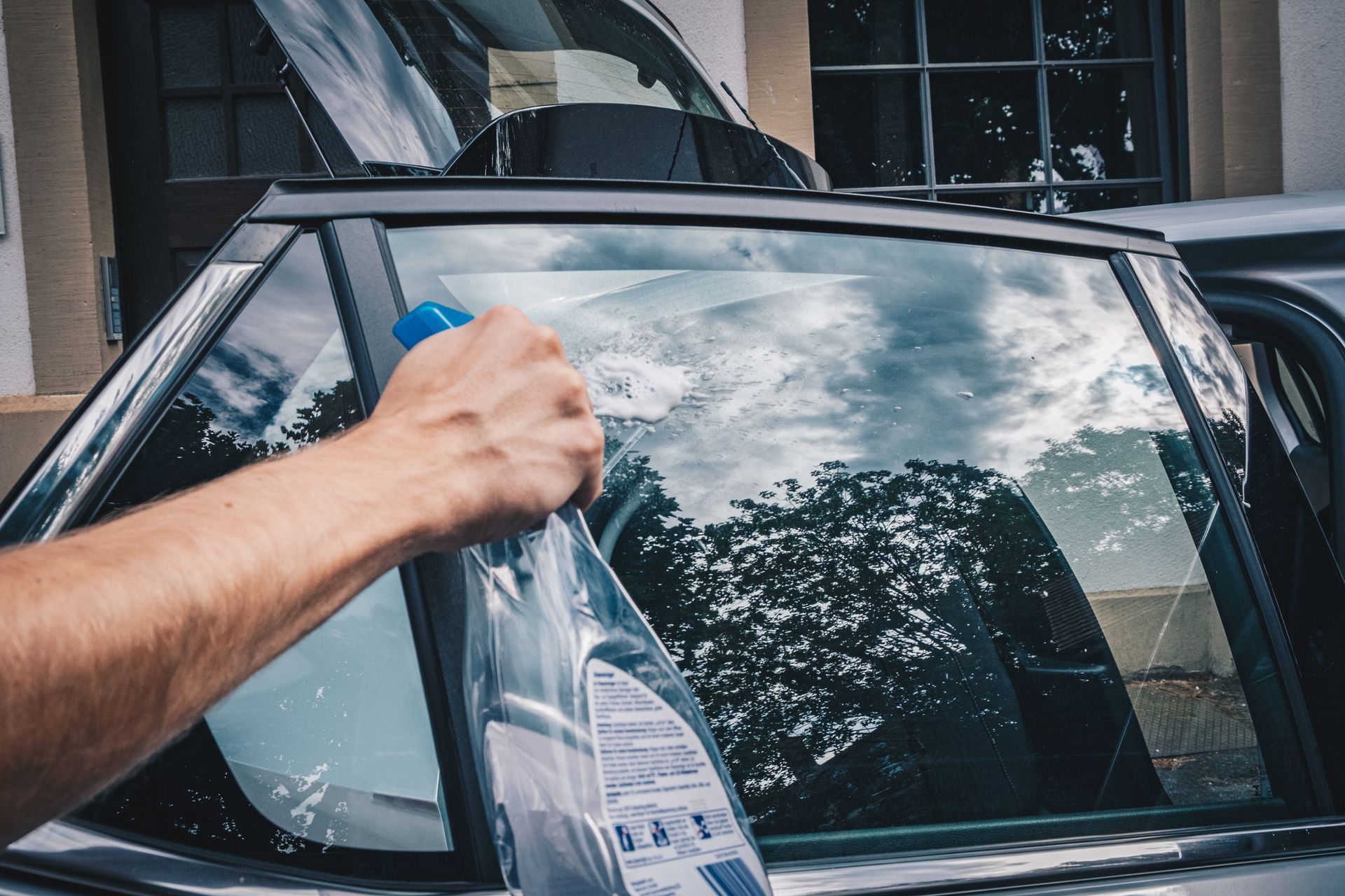 Young man prepares electric car for auto window tinting by cleaning glass surface thoroughly. 