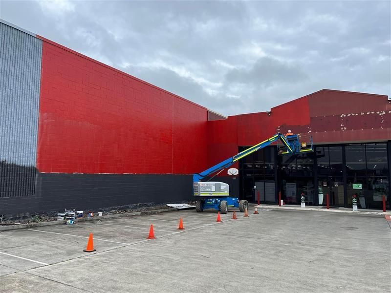 A man is painting the side of a building with a crane.