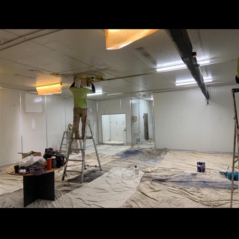 A man is standing on a ladder in a room painting the ceiling.