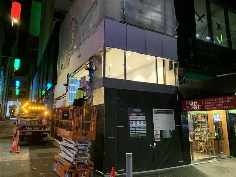 A man is standing on a scissor lift in front of a building.