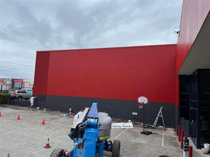 A red and black building is being painted in a parking lot.
