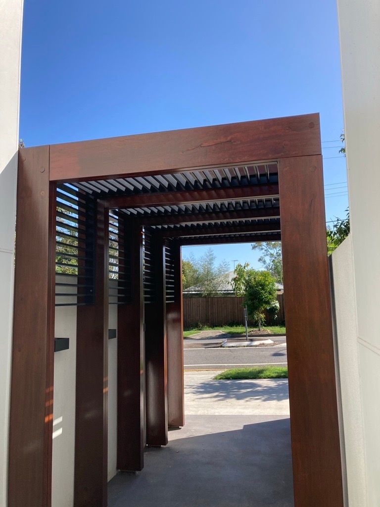 A wooden archway leading to a house with a blue sky in the background.