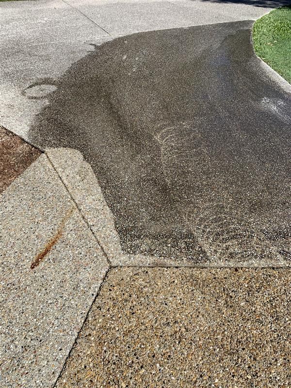 A close up of a concrete driveway with a shadow of a car on it.