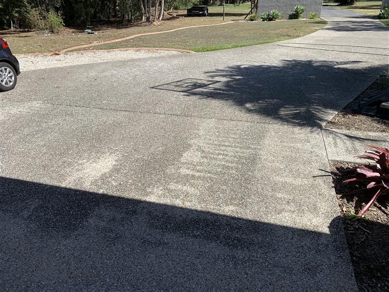 A concrete driveway leading to a house with trees in the background.