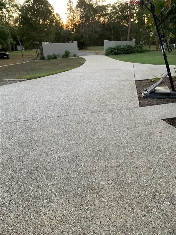 A concrete driveway leading to a house with trees in the background.