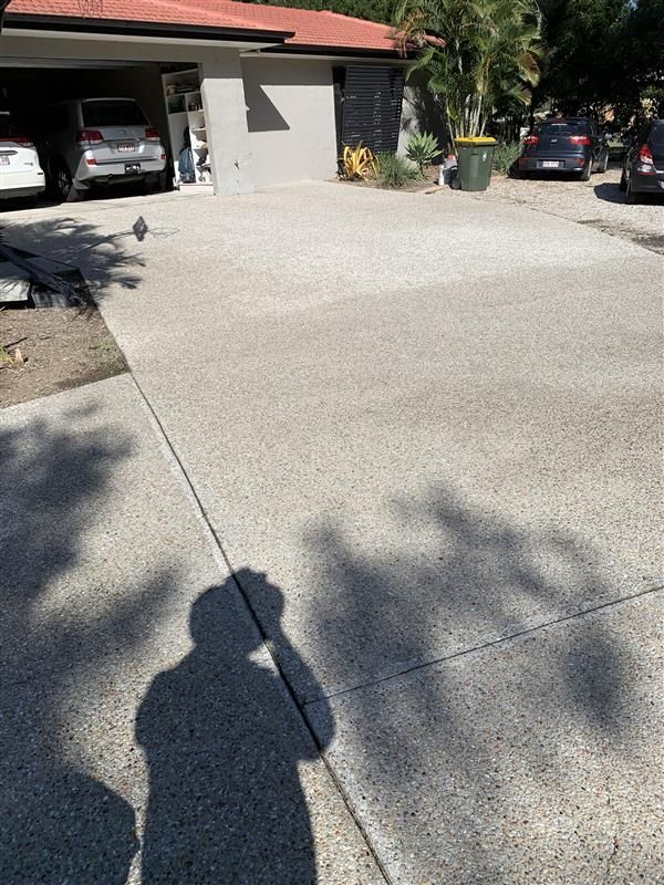A shadow of a person is cast on a concrete driveway in front of a house.