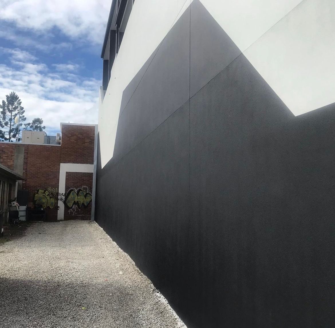 A black and white building with a gravel driveway leading to it