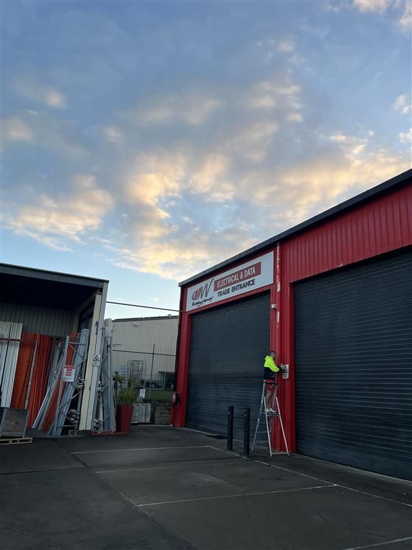 A man is standing on a ladder in front of a red building.