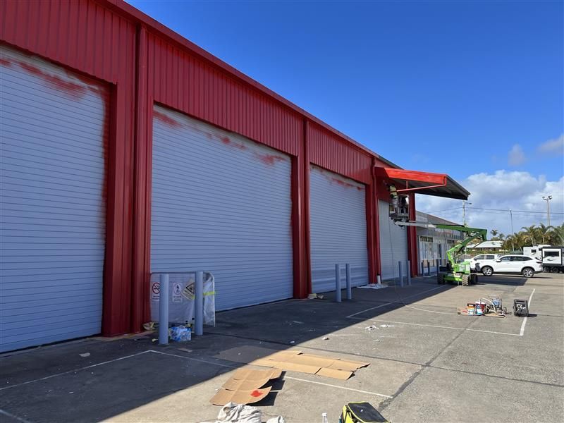 A red building with white garage doors is being painted.