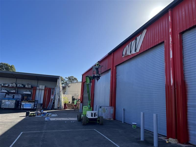A green crane is painting the side of a red building.
