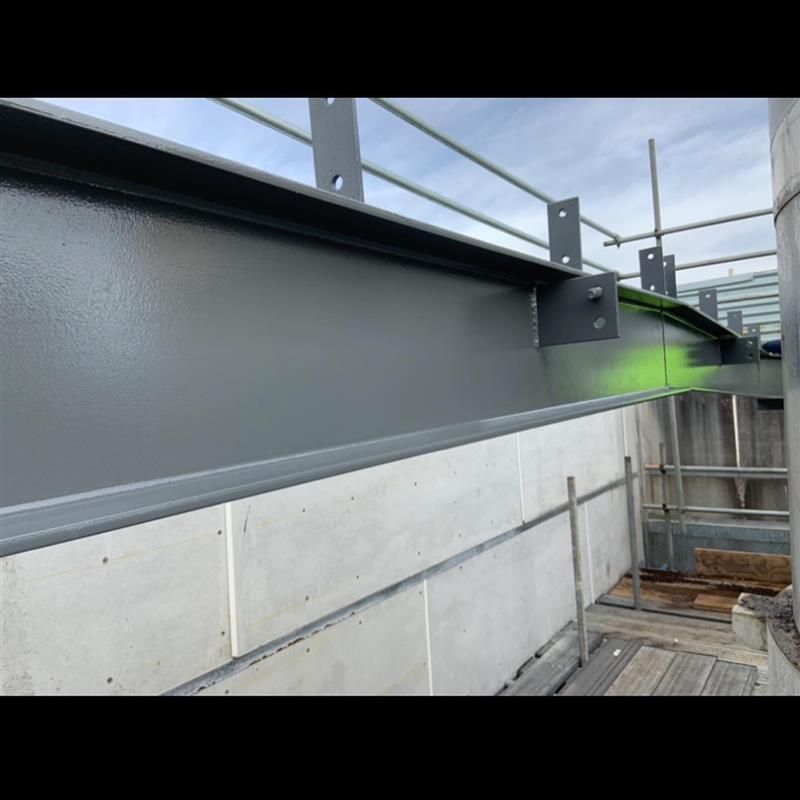 A gray metal beam is sitting on top of a concrete wall.