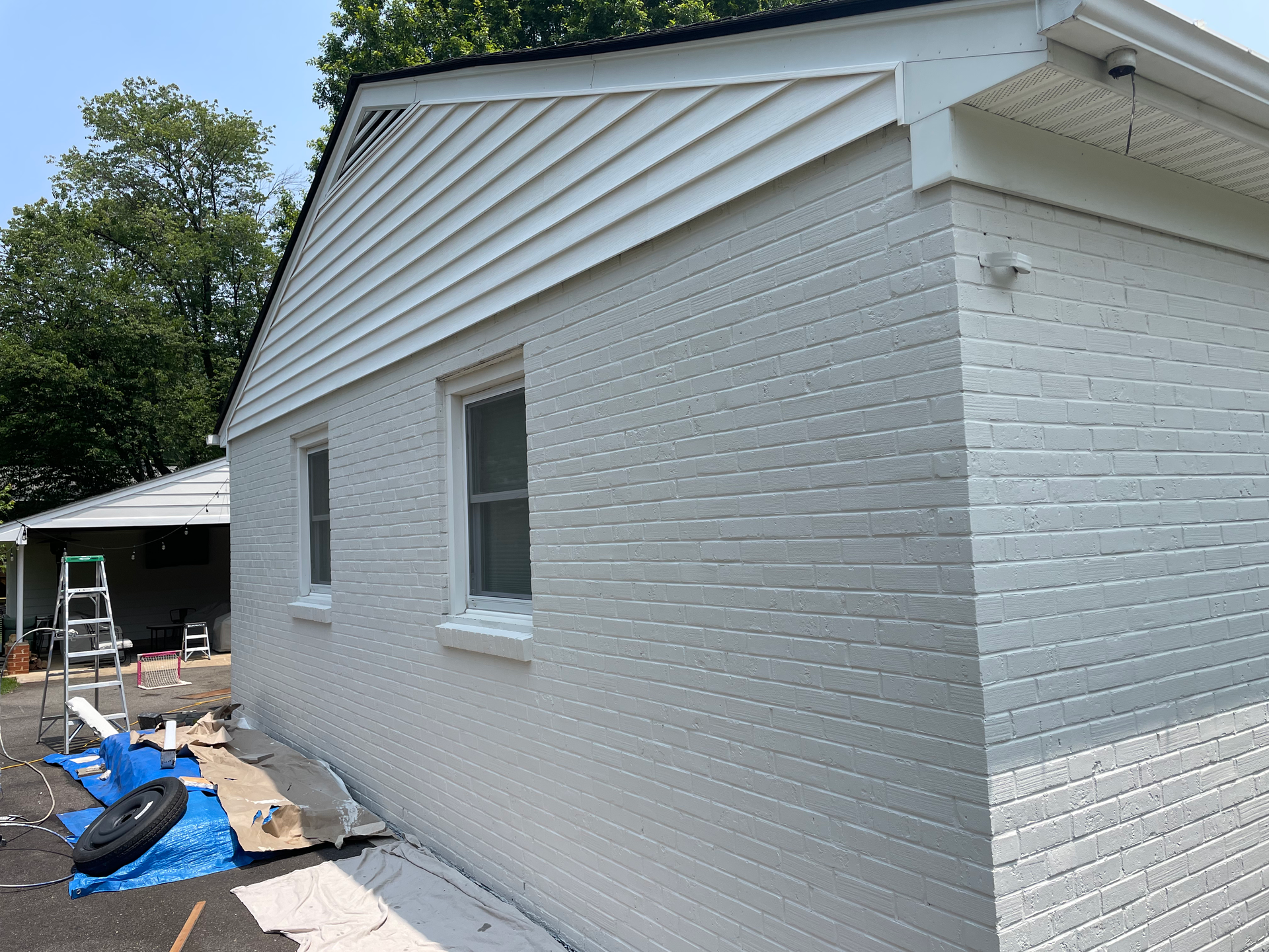 White painted brick house with a white siding gable, two windows, and a detached garage.