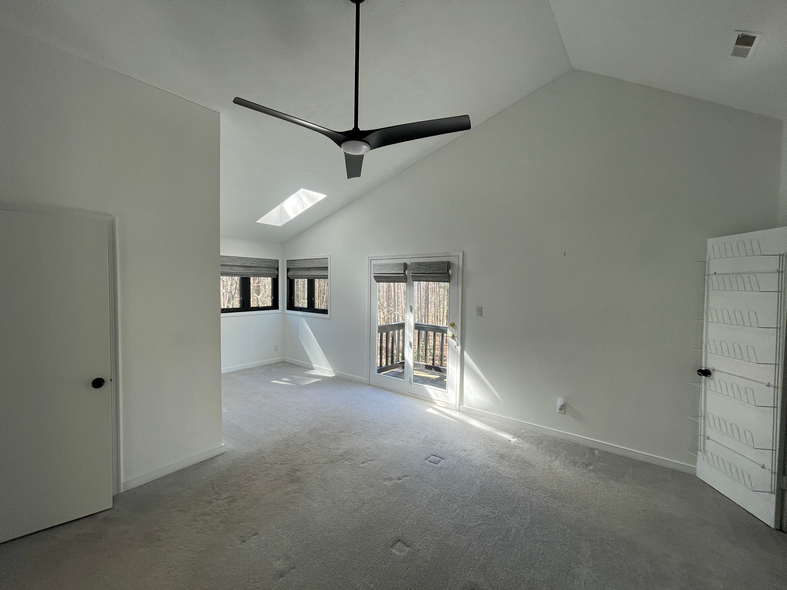 Empty bedroom with high ceilings, skylight, and sliding doors leading to a wooded view.