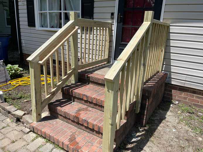 Wooden handrail and steps leading to a doorway of a house with a brick base.