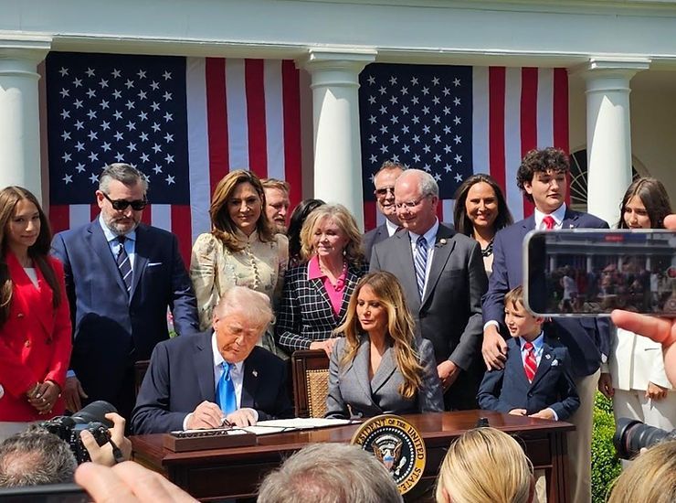 A group of people are standing around a table with a man in a suit signing a document.