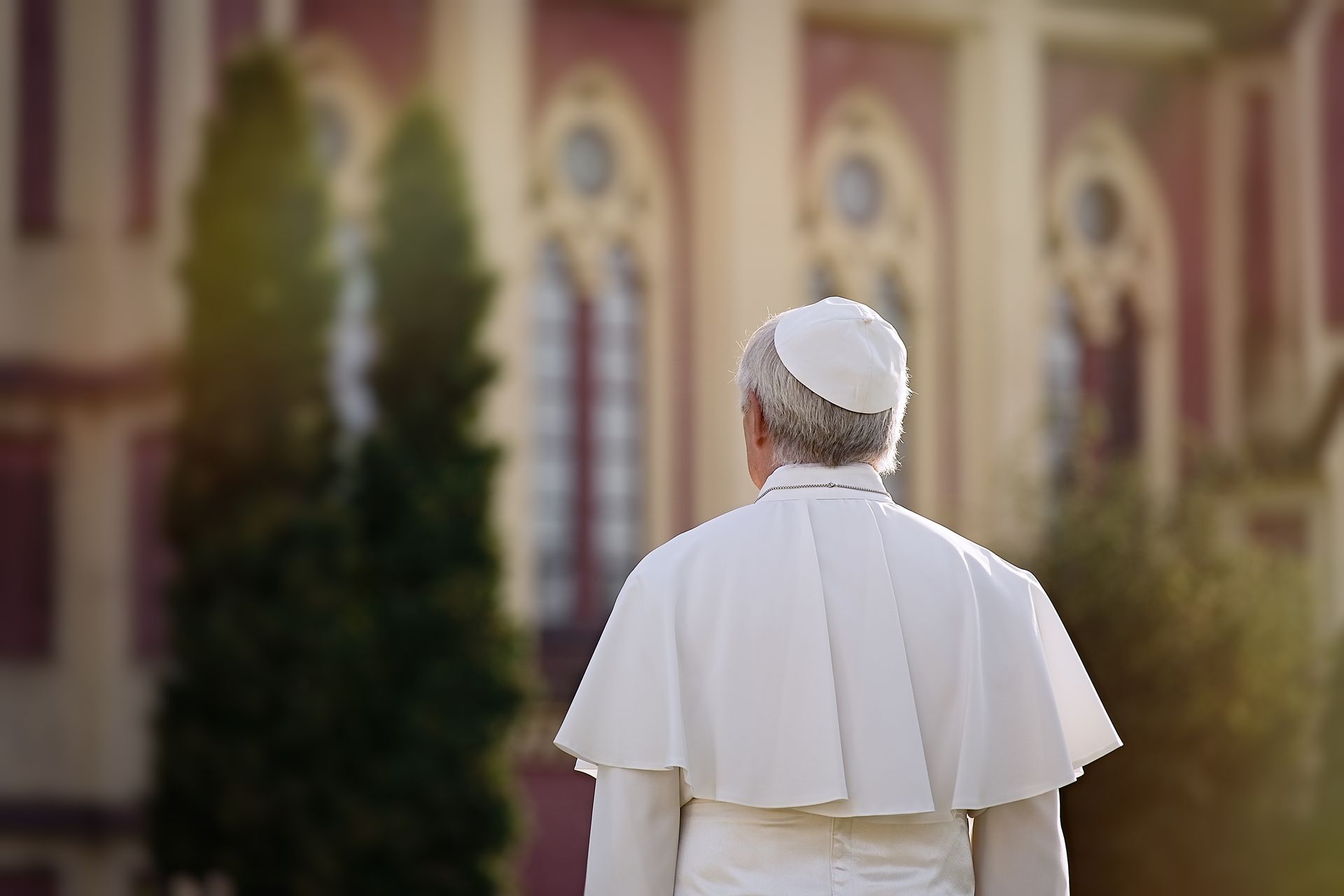 A man in a white robe is walking in front of a building.