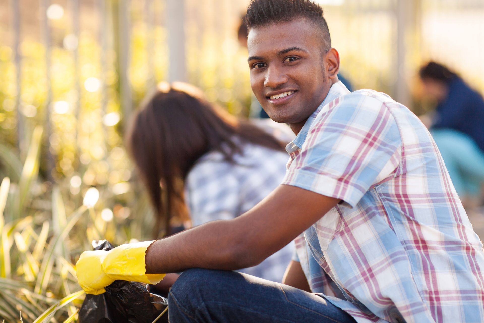 A man wearing yellow gloves is kneeling down in the grass.