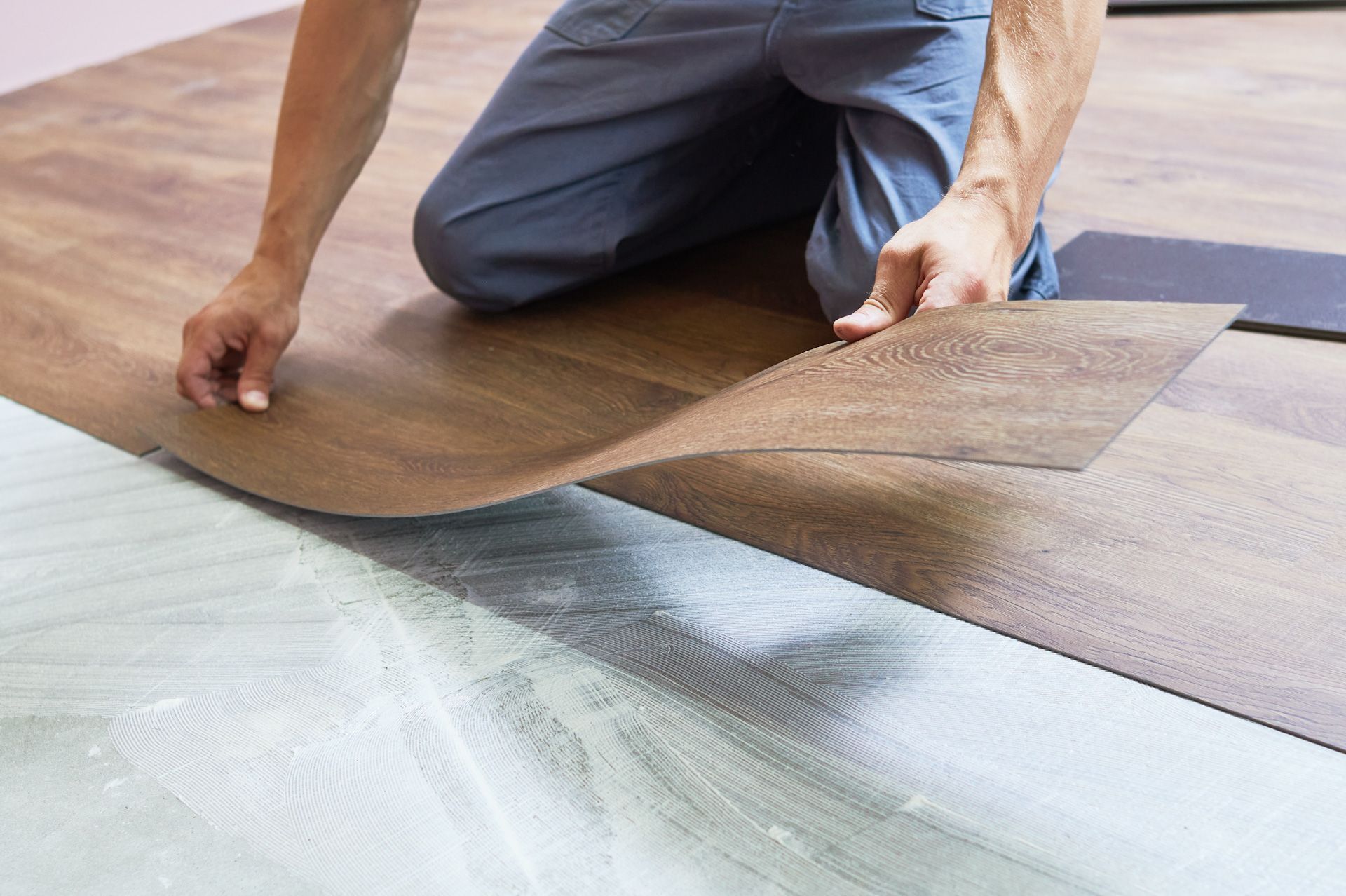A man is kneeling down to install a wooden floor.